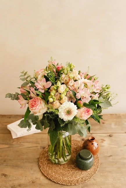 Vase de fleurs roses et blanches trônant au centre d une table en bois, accompagné de deux petites poteries et une enveloppe blanche.