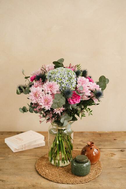 Un vase de fleurs colorées repose sur une table en bois avec des livres et des pots en céramique autour.