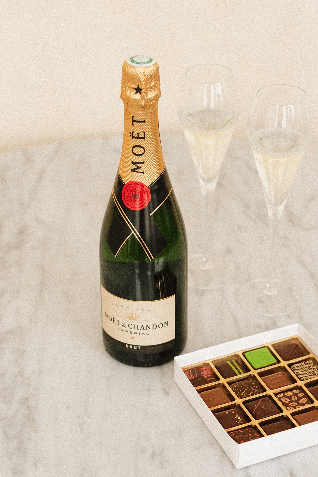 Bouteille de champagne Moët & Chandon et boîte de chocolats posées sur une table en marbre, accompagnées de deux flûtes de champagne.