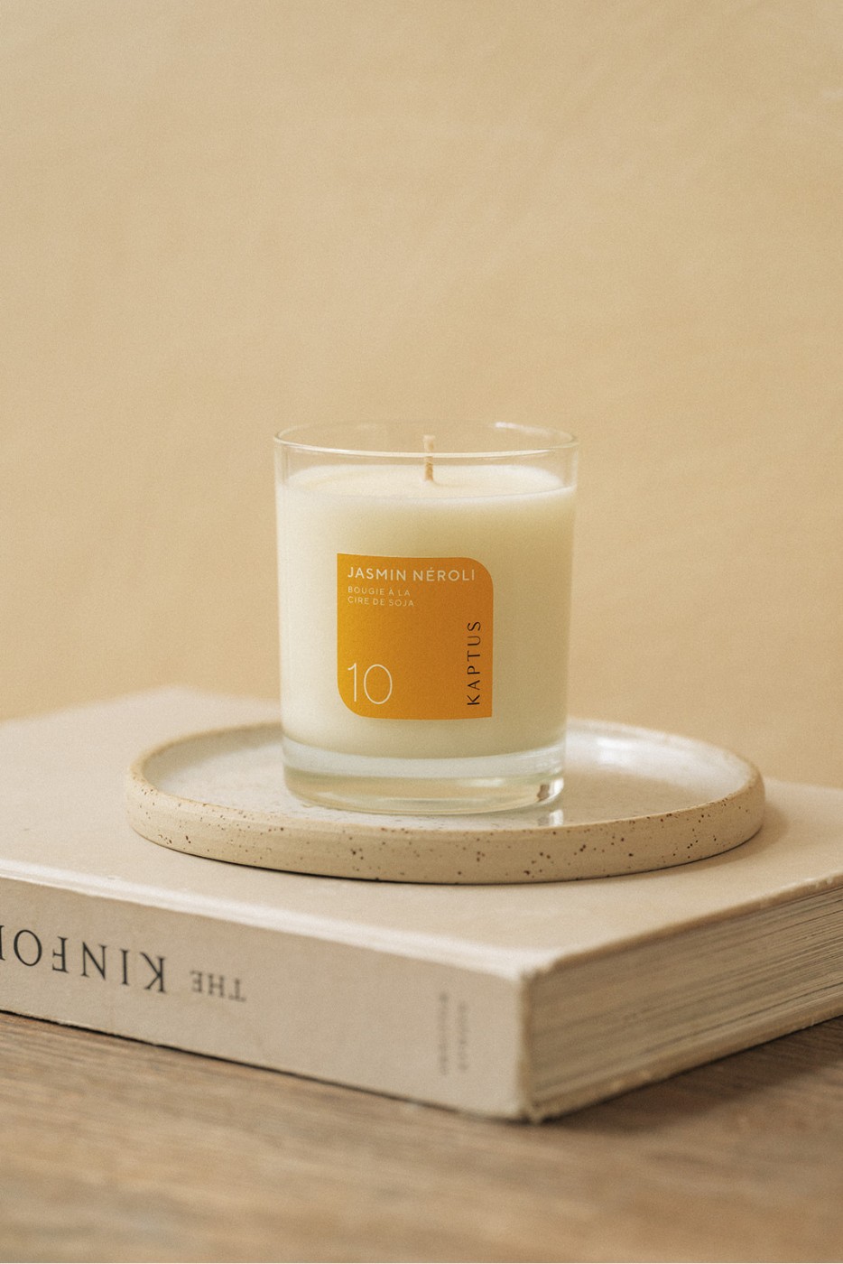 Bougie parfumée « Jasmin Néroli » en cire de soja, posée sur un plateau rond en céramique, lui-même sur un livre intitulé